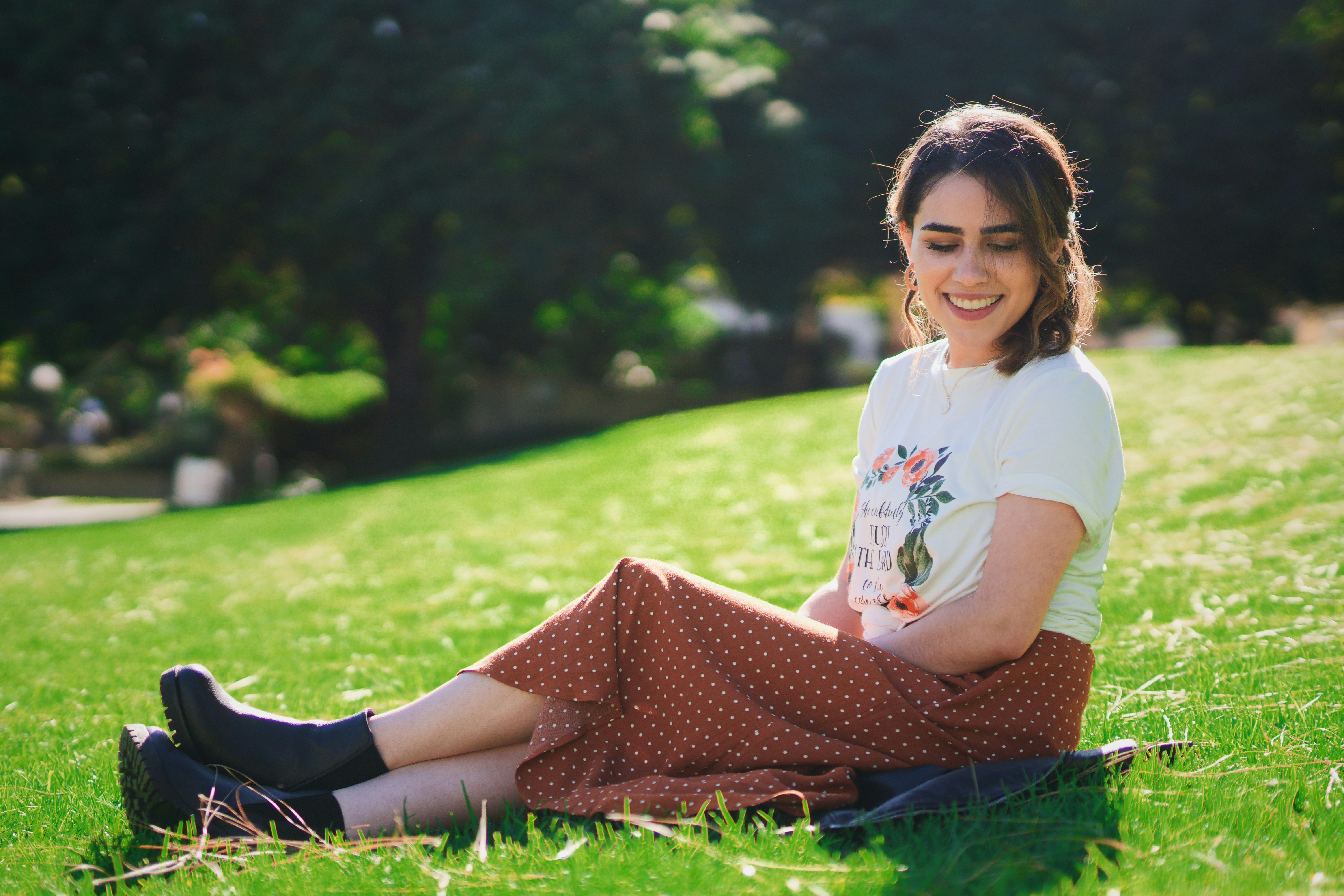 girl in white t-shirt and black pants sitting on green grass field during daytime